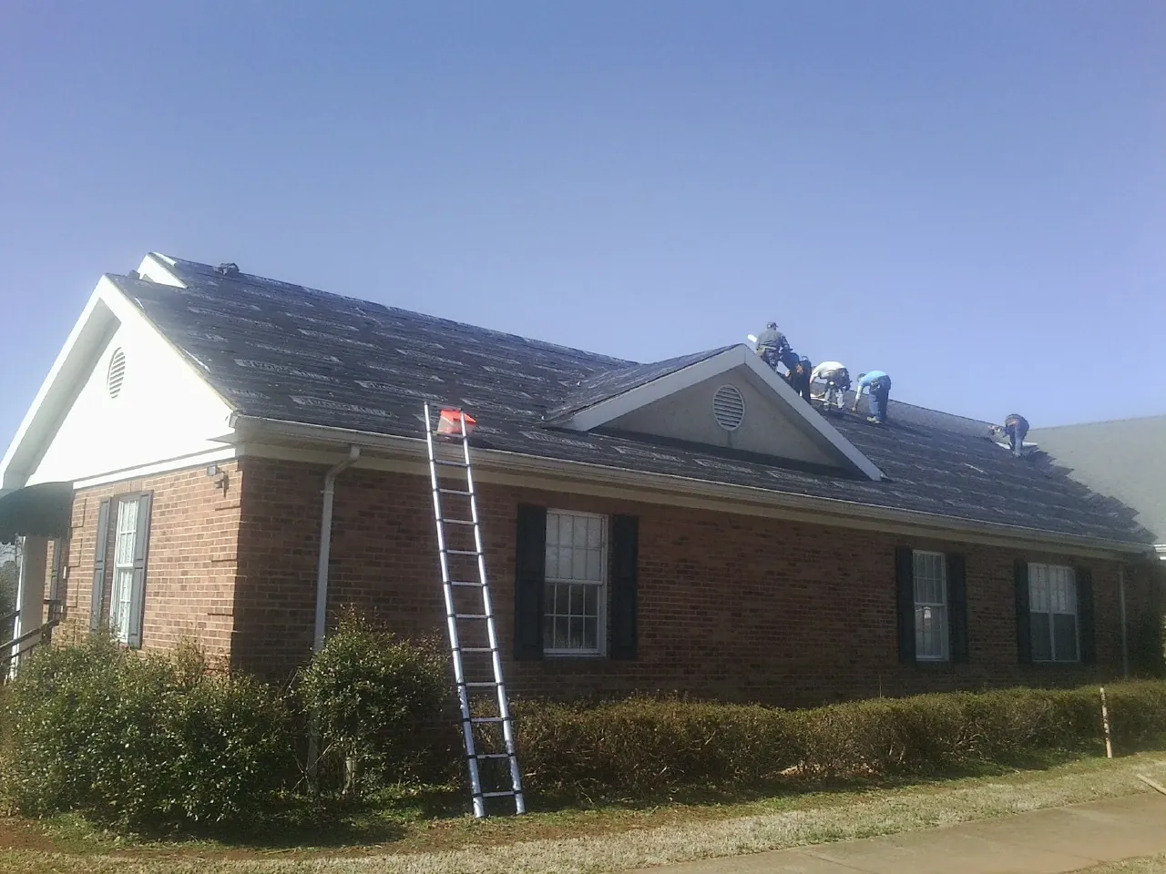 Crew tearing shingles off a brick ranch roof with a ladder set — Metal Roof Repair work by our crew in Washington Boro