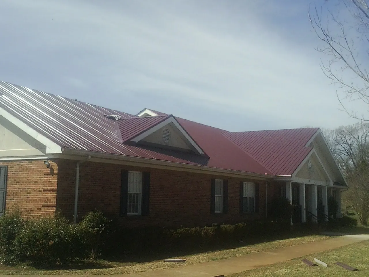 Red metal roof with gabled entries on a long brick building, from a Hail Damage Roof Repair job in Washington Boro