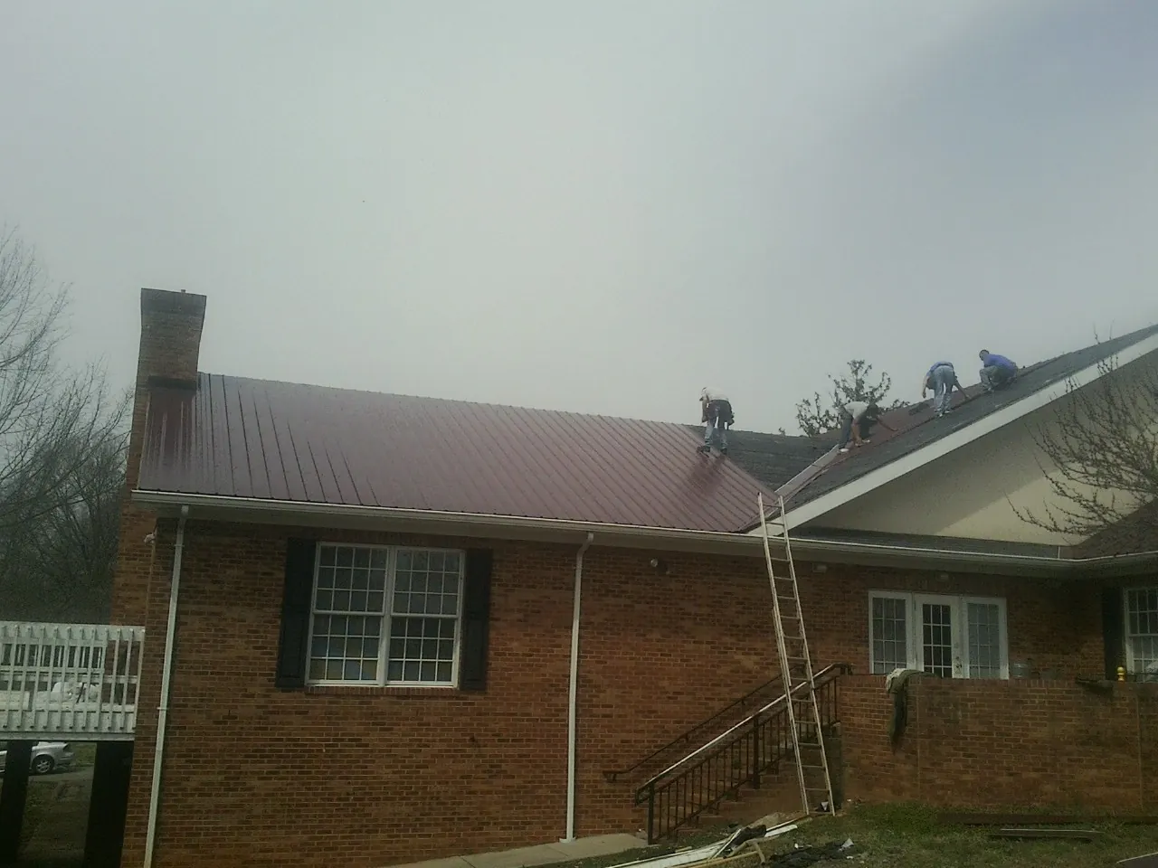 Crew setting red metal roofing panels on a brick home in Washington Boro