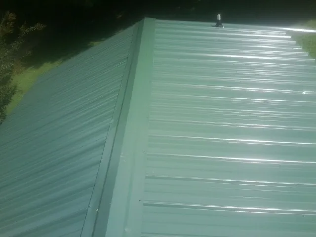 New green metal panels meeting at the ridge of a roof — Flat Roof Repair work by our crew in Washington Boro
