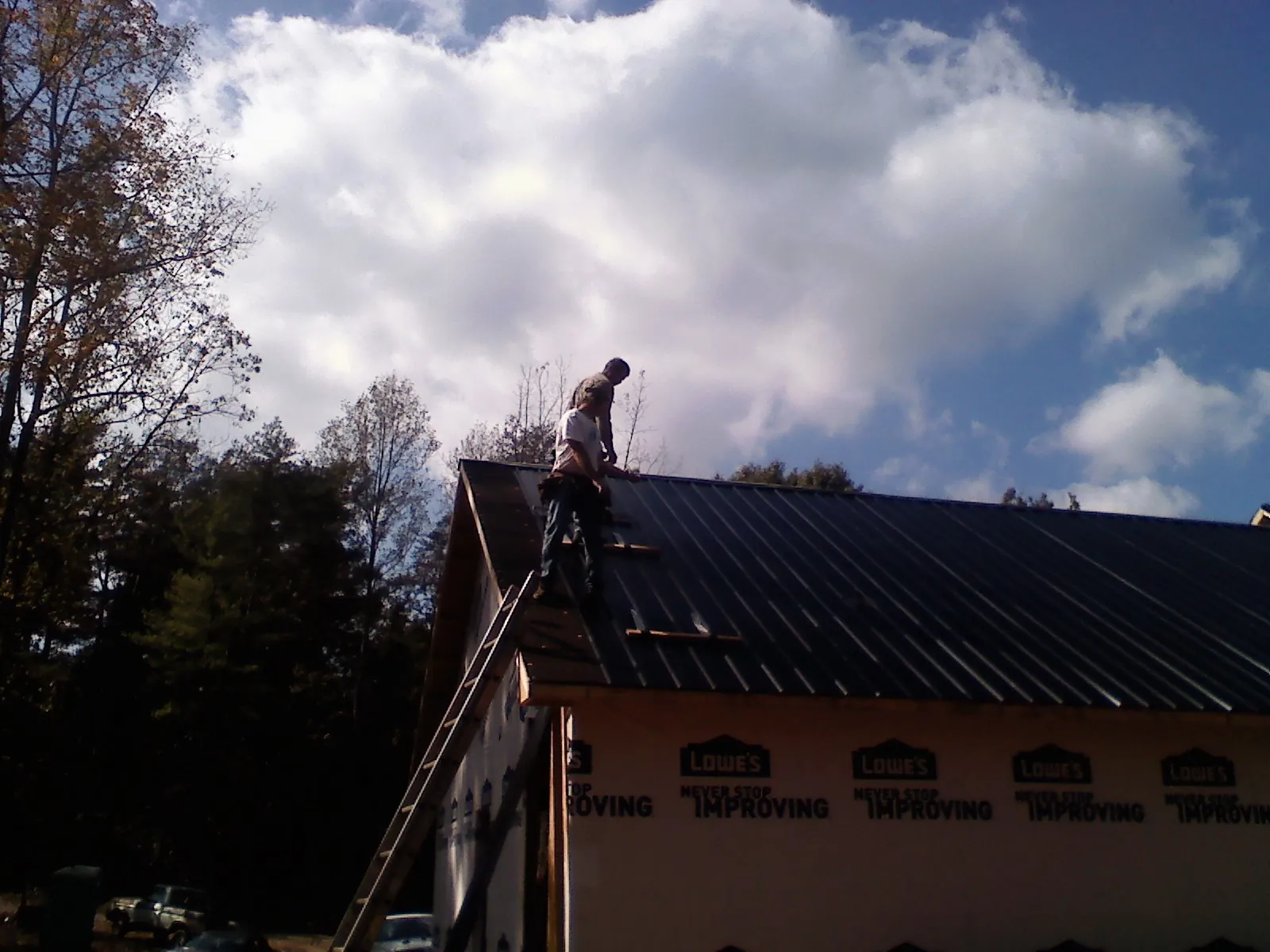 Roofer fastening dark metal panels high against a cloudy sky, from a Roof Inspection job in Washington Boro