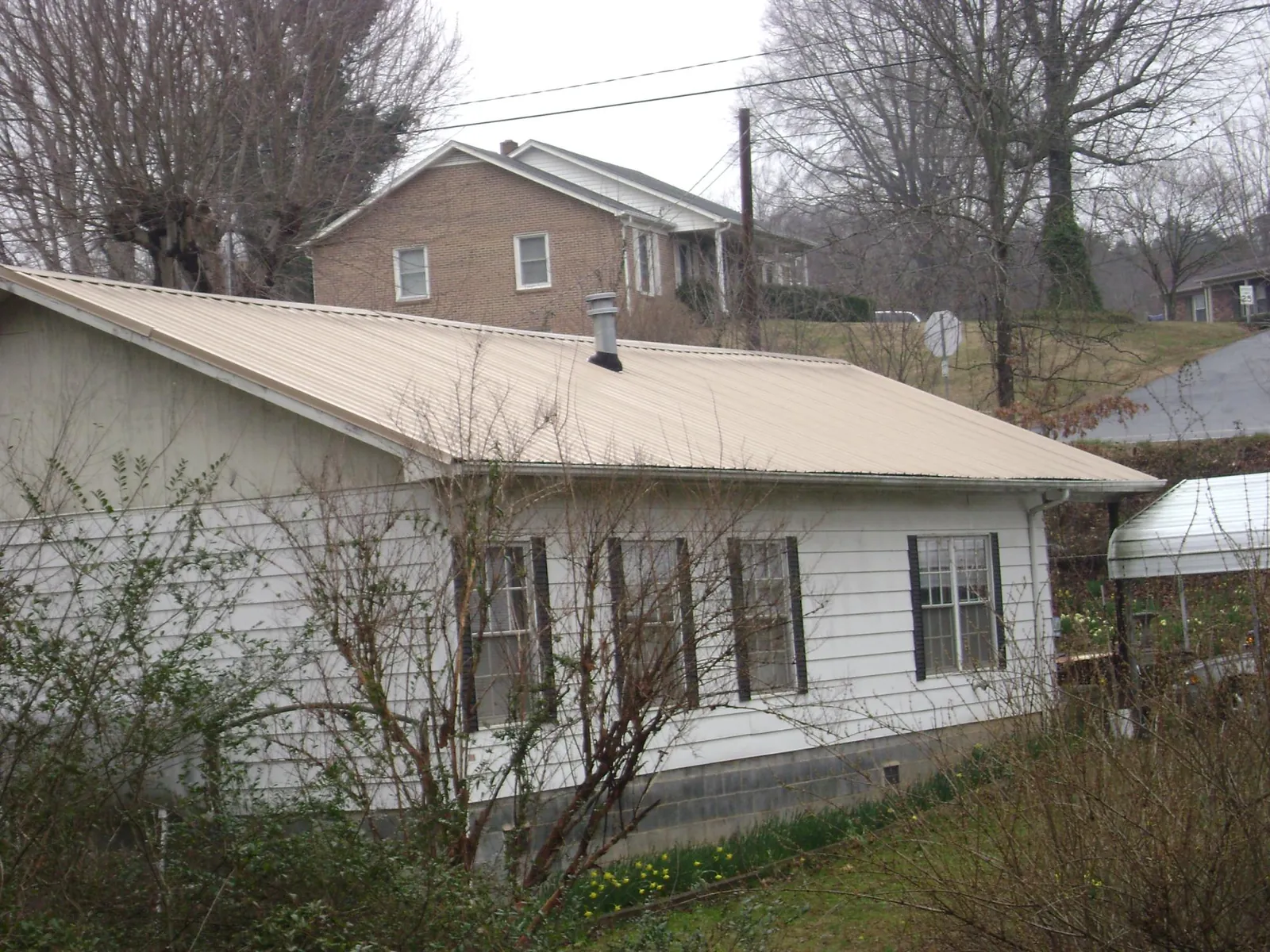 Tan metal roof on a white sided house set into a hillside — Commercial Roofing by Roofing Brothers in Washington Boro
